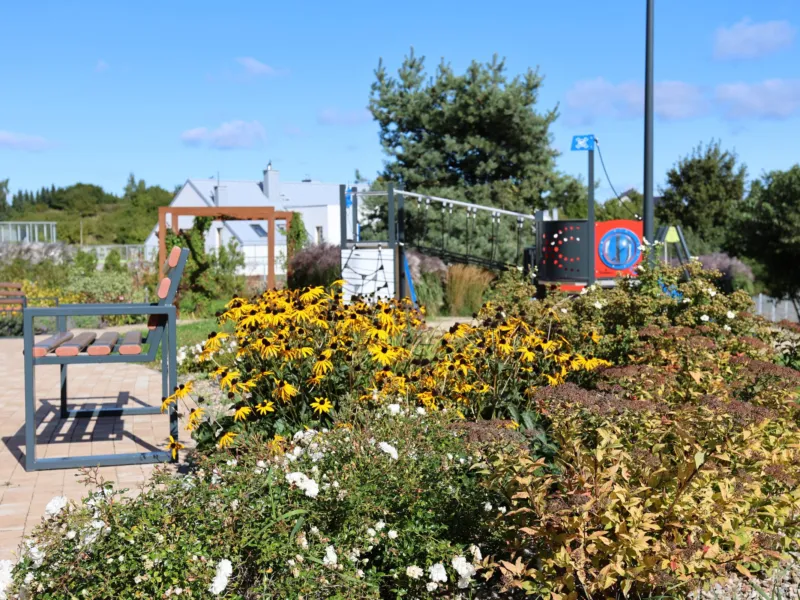 Rabaty kwiatowe i ławka przy placu zabaw w Brizo Park